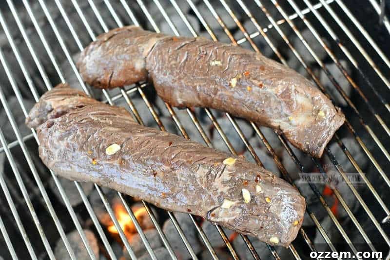 Fire Kissed Hanger Steak 6 Two long, marinated hanger steaks cooking over hot charcoal on a grill