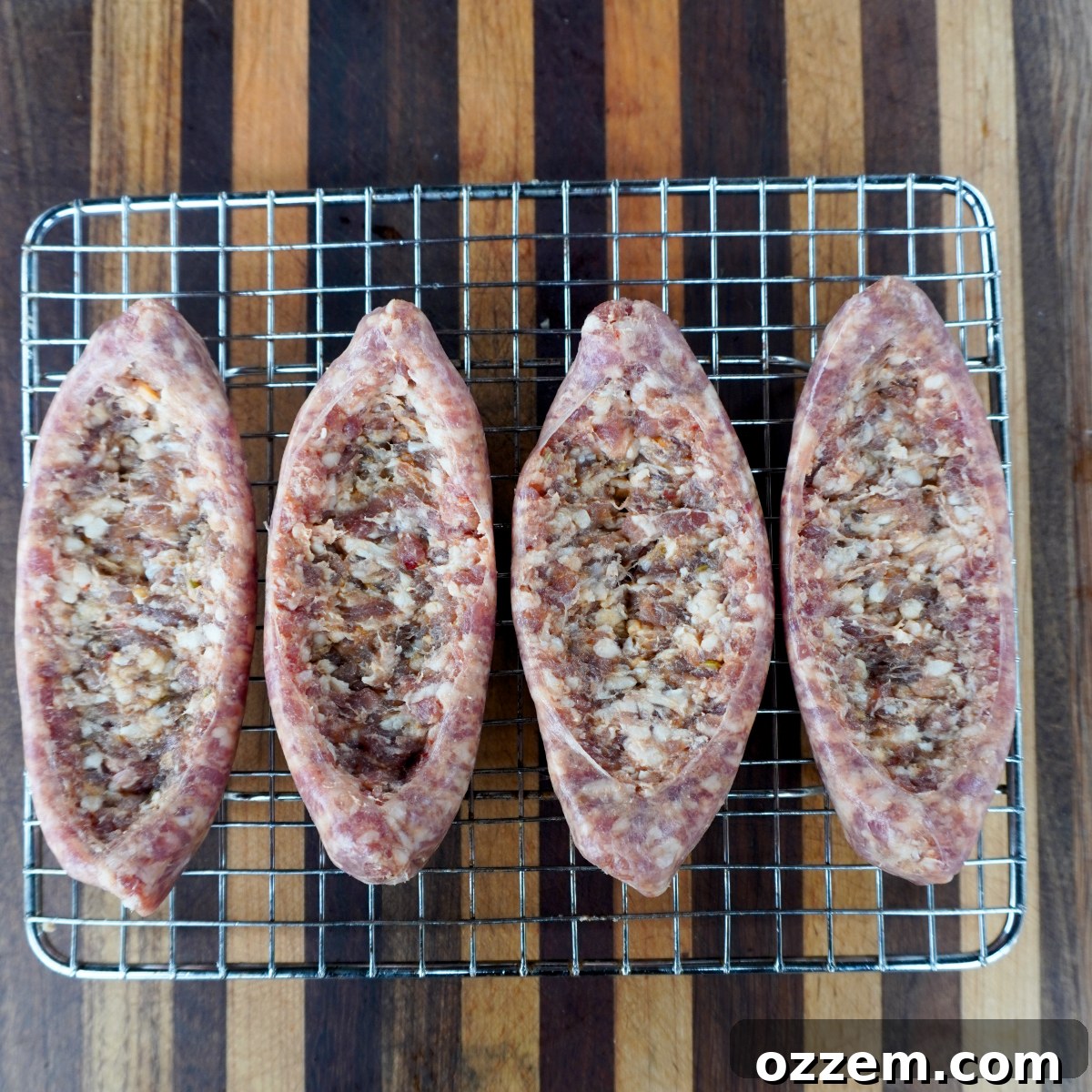 Four raw Italian sausages, expertly split and shaped into kayak-like boats, arranged neatly on a wire rack for preparation.