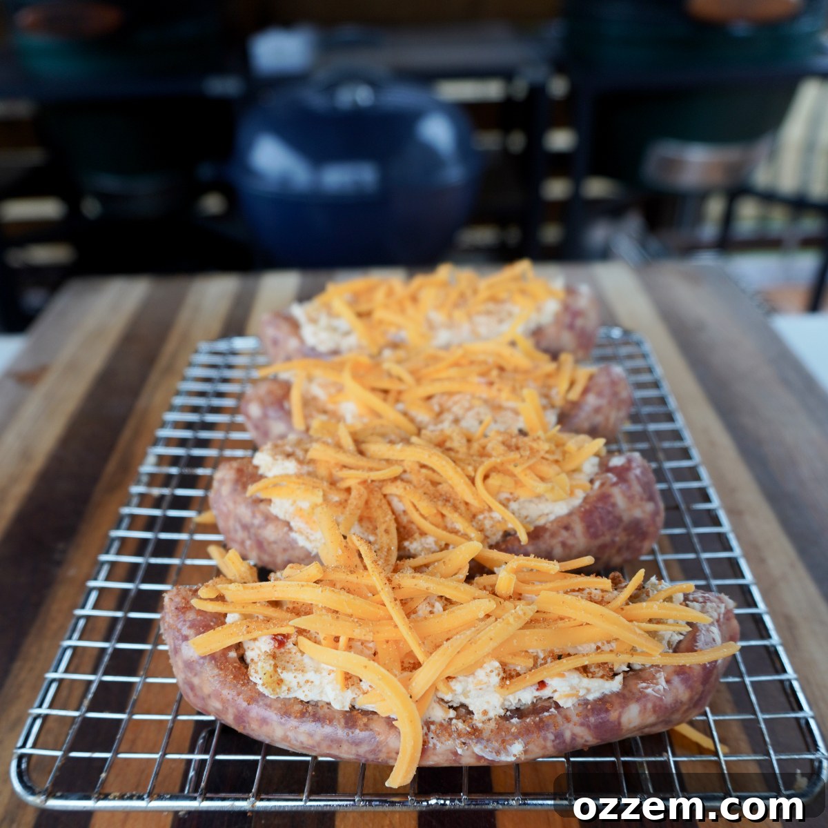 Italian sausage links expertly stuffed with a creamy cheese filling and generously topped with shredded cheddar cheese, all arranged on a wire rack, ready for cooking.