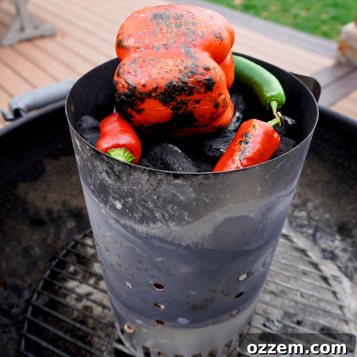 Red bell peppers, jalapeños, serrano pepper, and red onion roasting over hot charcoal, developing a smoky char.