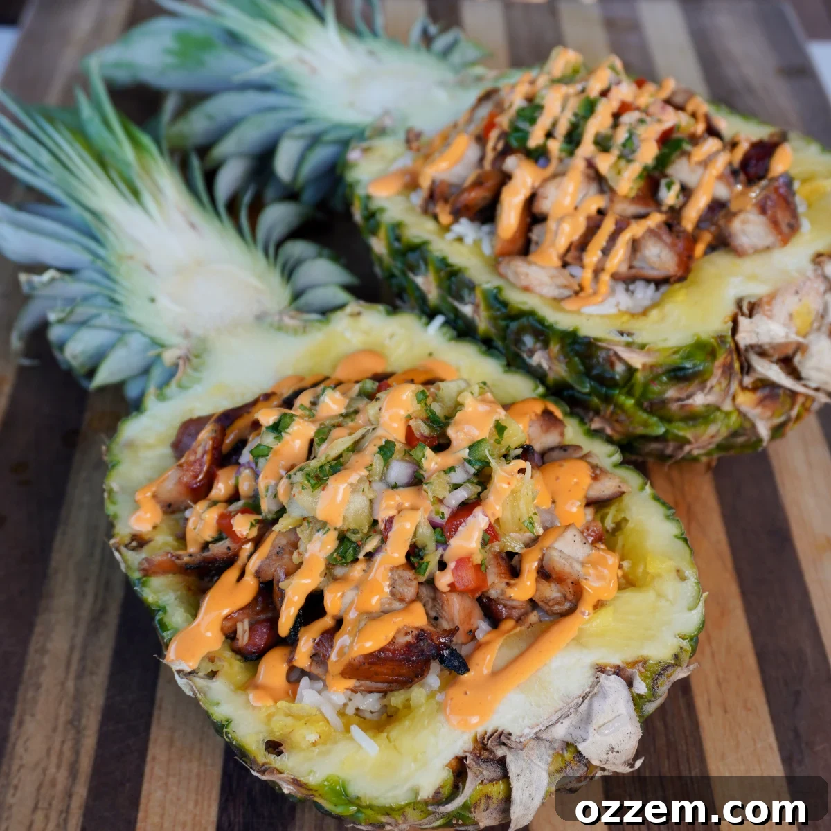Two halves of grilled teriyaki chicken boats in pineapple, filled with coconut rice and pineapple salsa, drizzled with sriracha mayo.