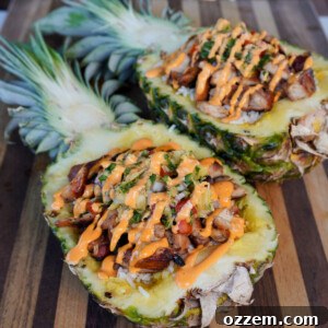 Two vibrant Teriyaki Chicken Bowls, served in hollowed-out pineapple halves, filled with coconut rice, grilled chicken, pineapple salsa, and sriracha mayo.