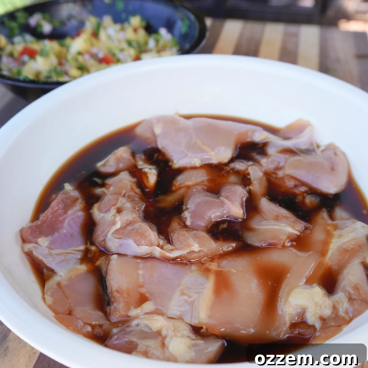 Chicken thighs marinating in teriyaki sauce in a glass bowl.