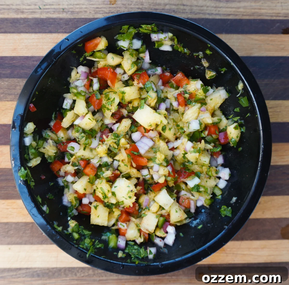 Close-up of freshly made pineapple salsa in a bowl with chopped ingredients like pineapple, red bell pepper, red onion, and cilantro.