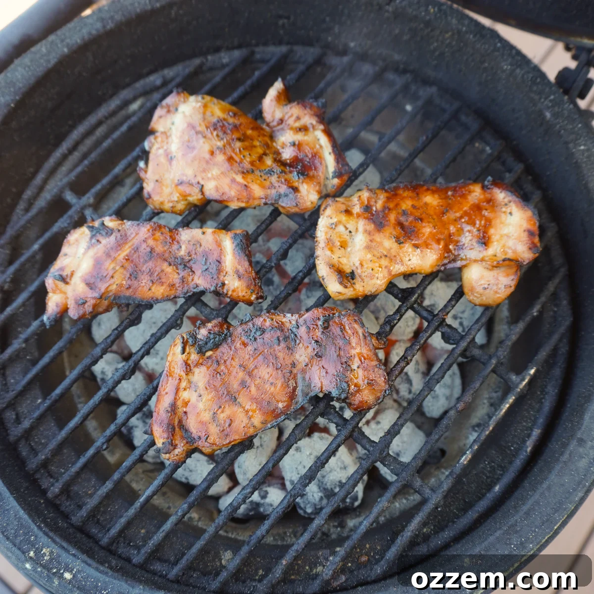 Teriyaki chicken thighs grilling over direct heat on a barbecue, showing char marks.