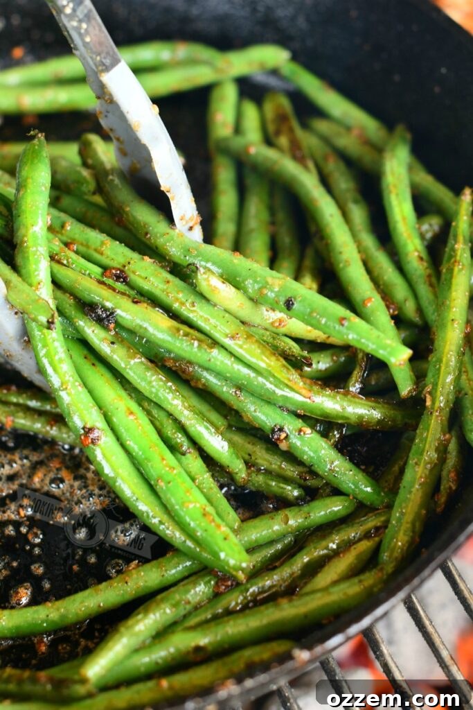 using metal tongs to scoop green beans in a skillet