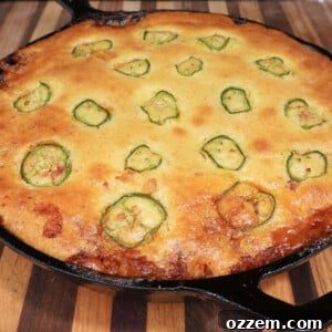 A close-up shot of a savory Cornbread Cowboy Casserole in a cast iron skillet, with a scoop removed to showcase the hearty layers of beef, beans, and corn beneath a golden cornbread crust.