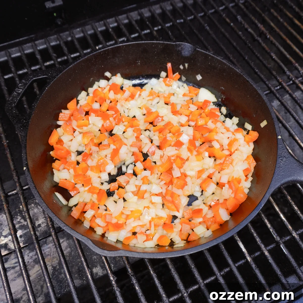 Freshly sauteed red bell peppers, yellow onions, and minced garlic simmering in a cast iron skillet over high heat on a backyard grill.