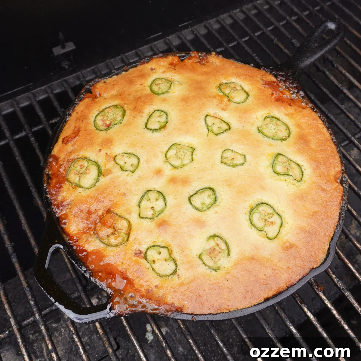 A glorious smoked cornbread cowboy casserole, bubbling and golden brown, still in its cast iron skillet on a hot grill, ready to be served.