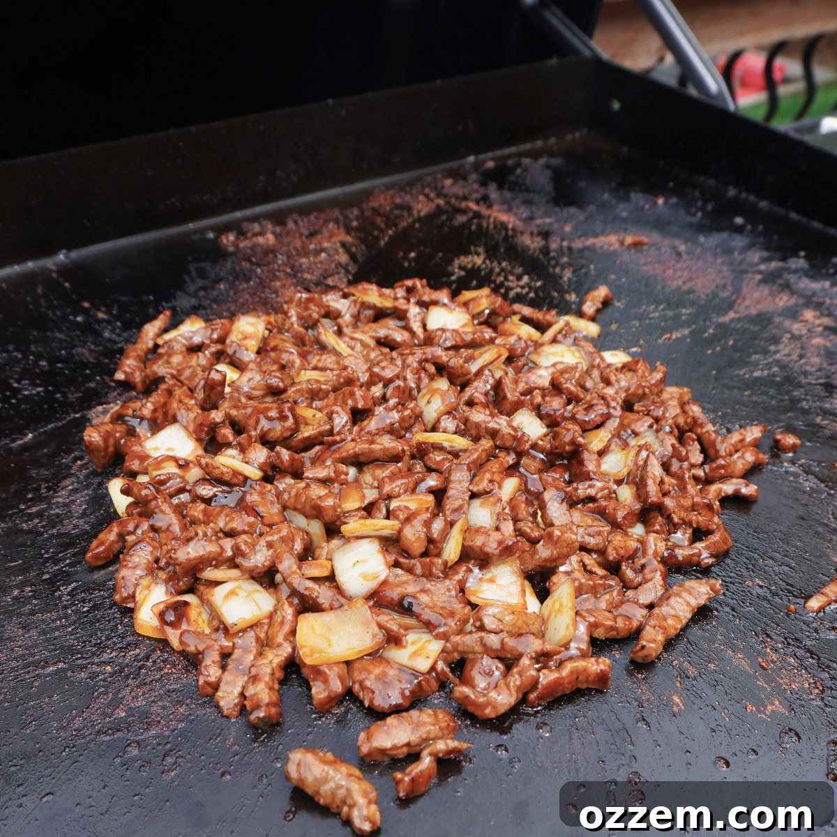 Spicy Teriyaki Beef and onions sizzling on a flat top grill