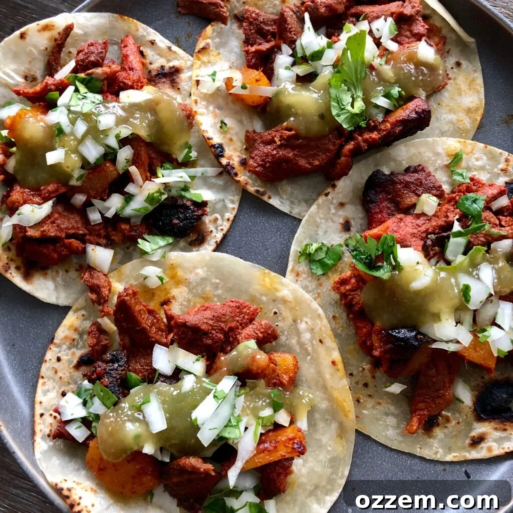 Close-up of freshly assembled al pastor tacos with cilantro, onion, and salsa on warm tortillas.