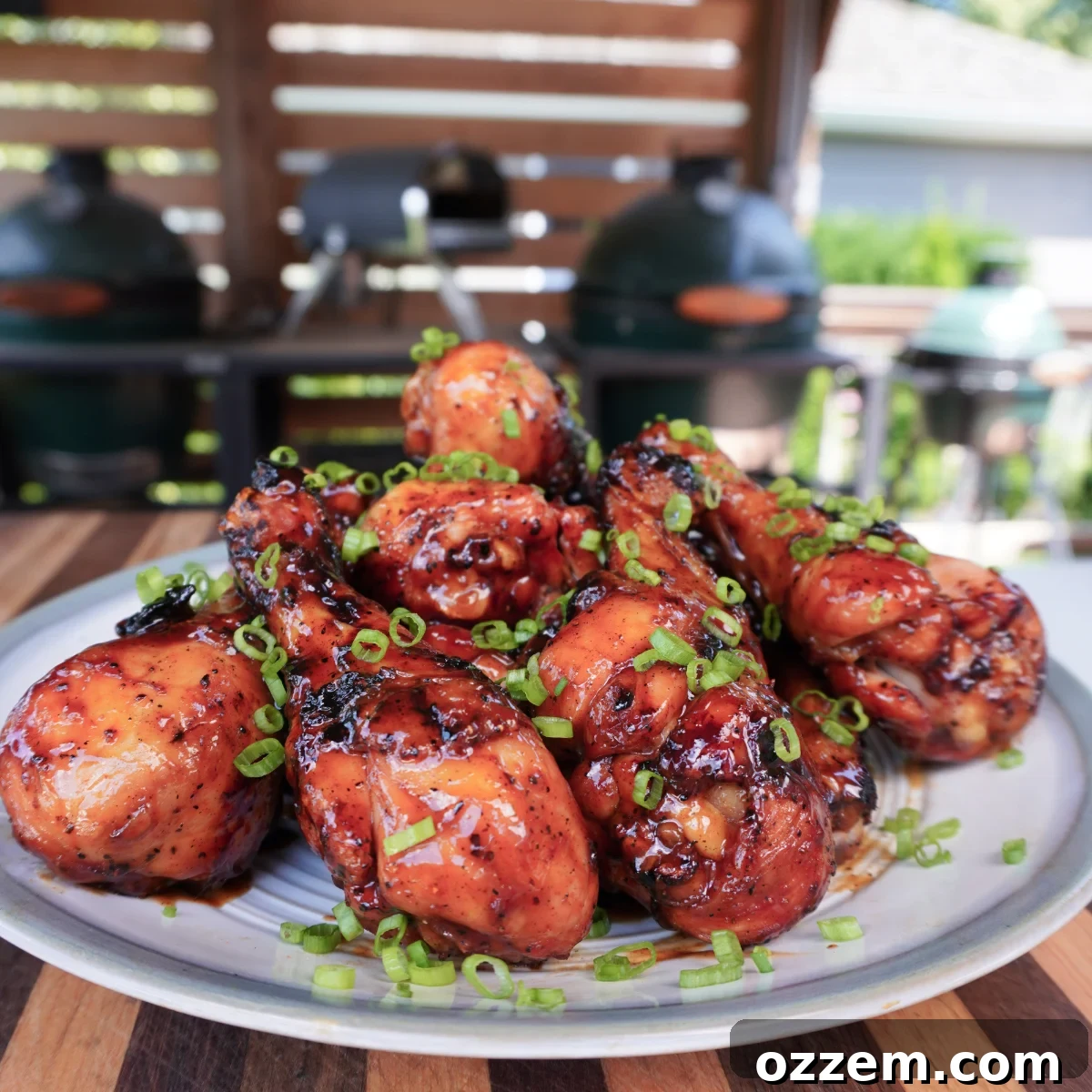 A pile of grilled chicken drumsticks in Dr Pepper BBQ sauce on a place with grills in the background.