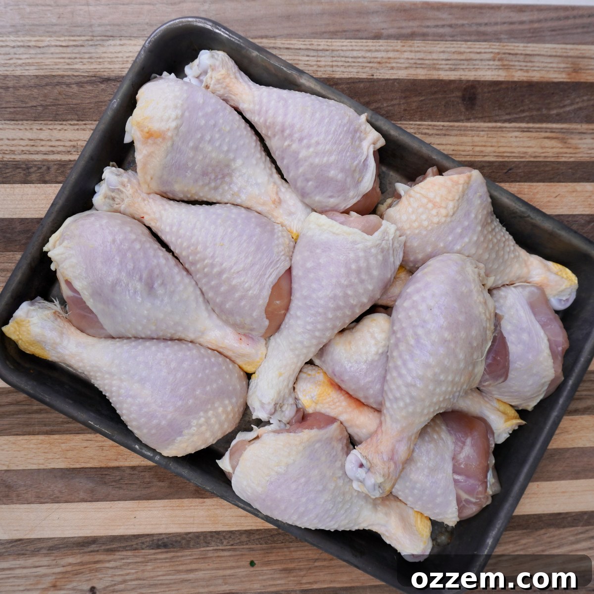 Raw chicken drumsticks on a metal tray.