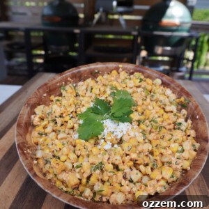 A bowl of creamy grilled corn salad, garnished with fresh cilantro and a lime wedge.