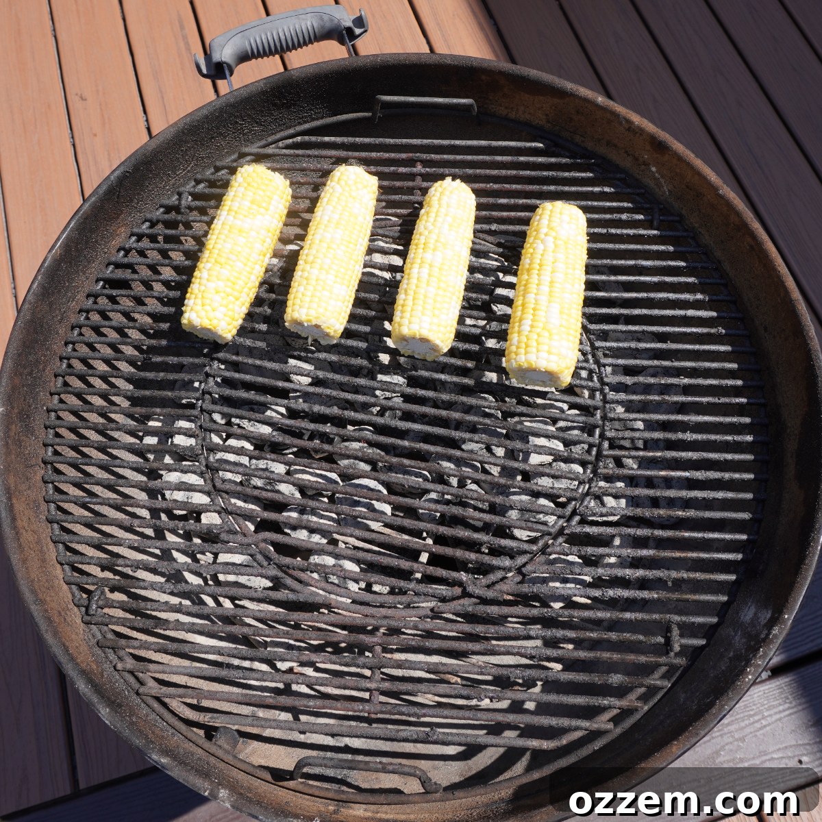 Grilled corn cobs arranged on a hot grill, showing smoky char marks