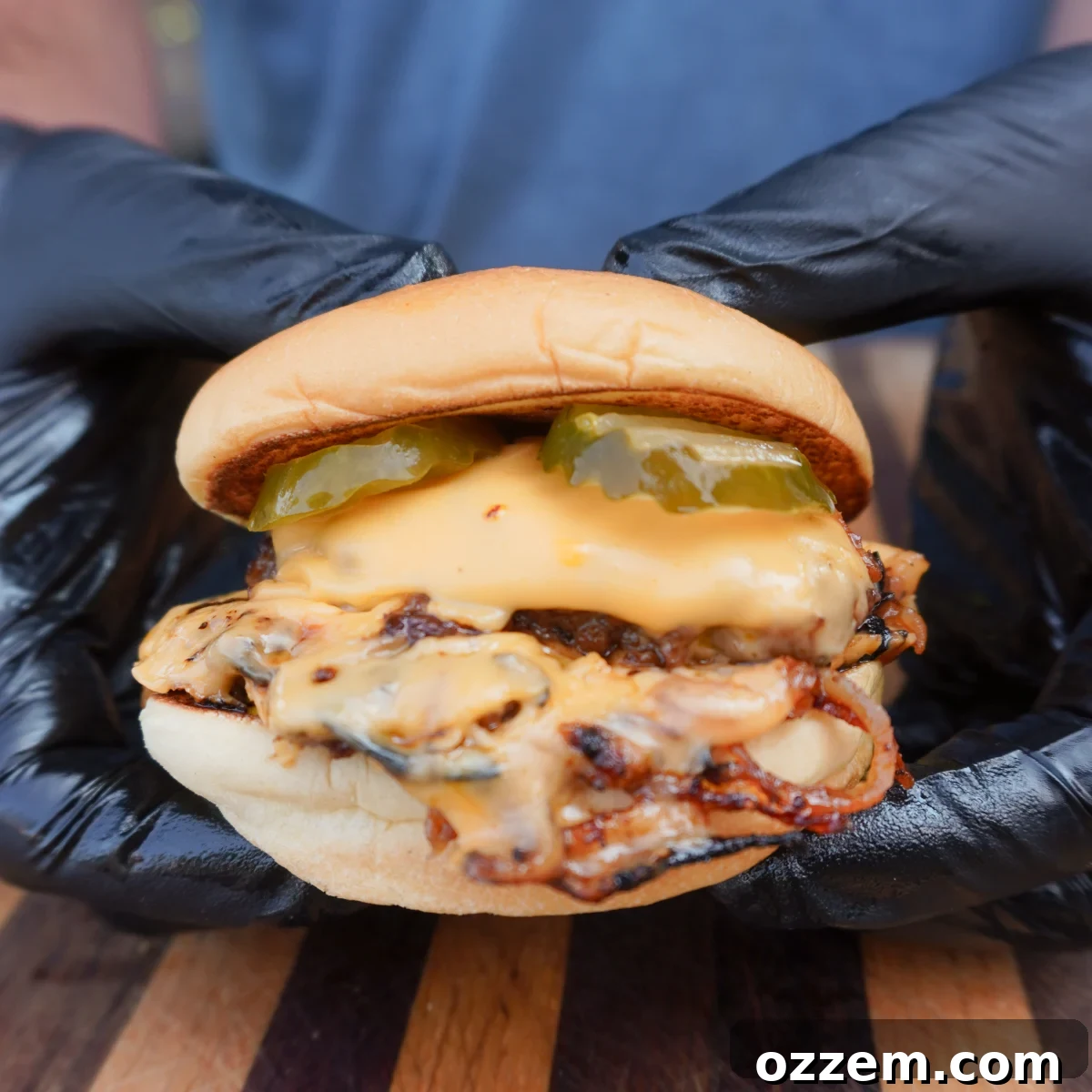 An assembled Oklahoma Onion Burger held by 2 hands, showcasing its juicy patty and crispy onions.