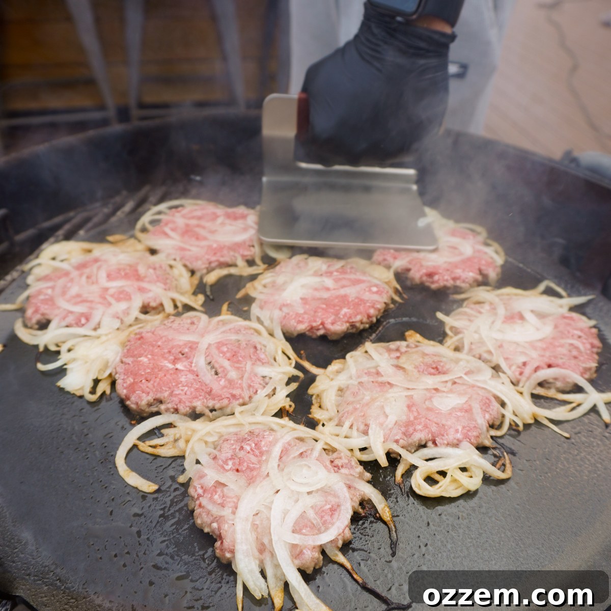 Oklahoma onion burger patties being smashed down on a griddle with a spatula.