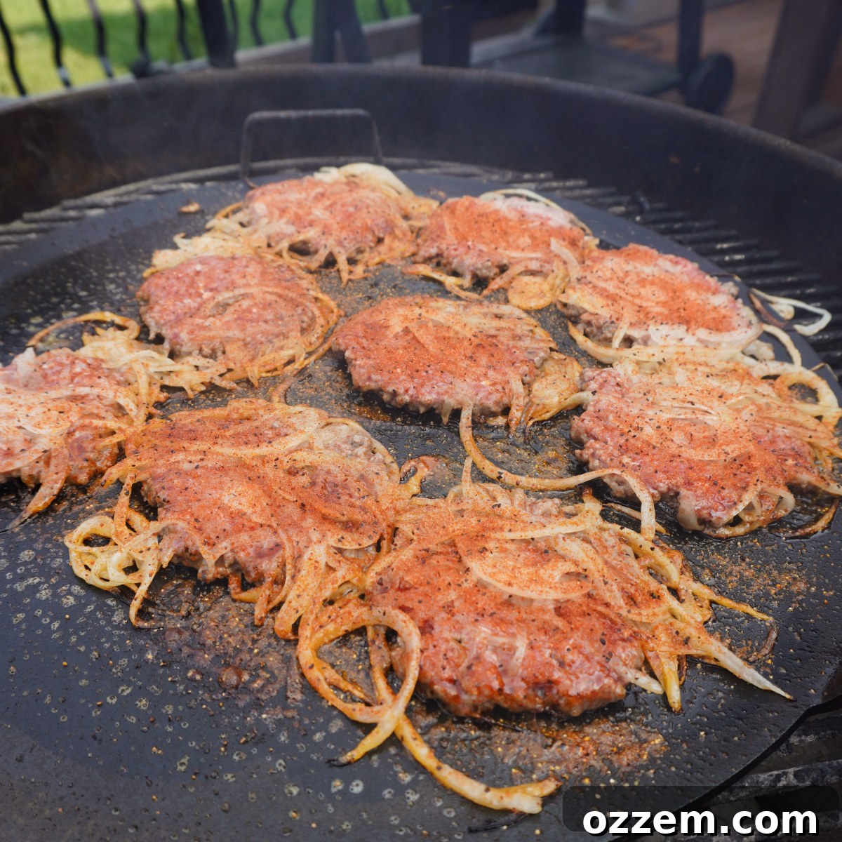 Seasoned smashed beef and onion patties cooking on a griddle, browning beautifully.