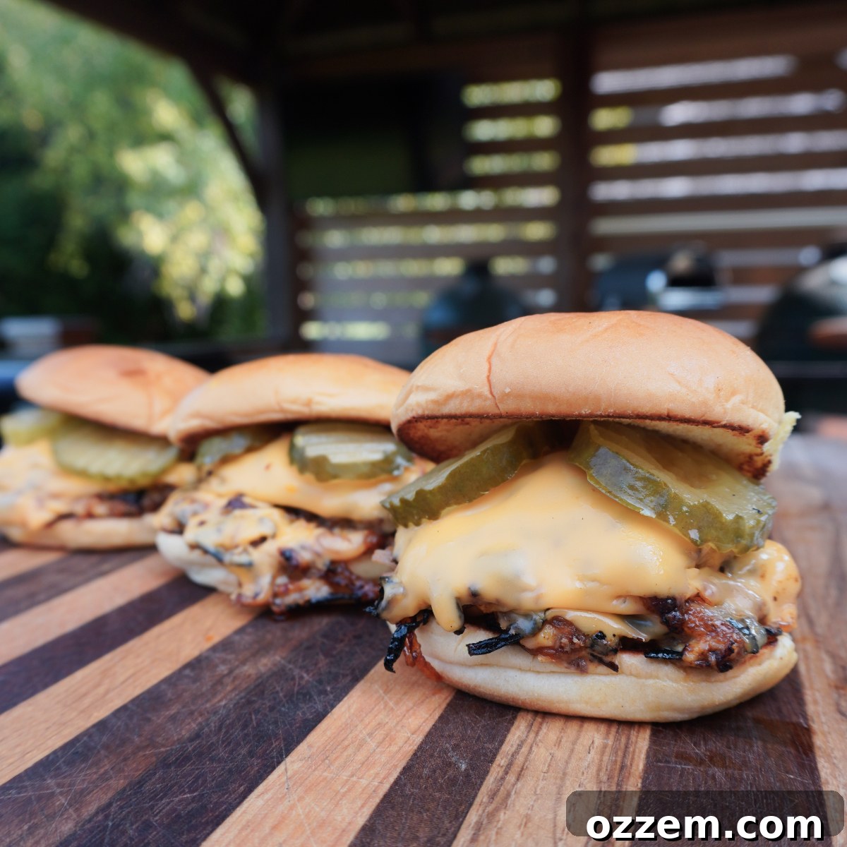 Three fully assembled Oklahoma Onion Burgers on a wooden cutting board, ready to be enjoyed.