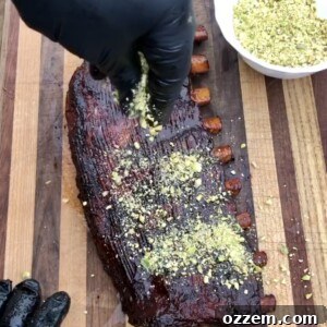 Crushed pistachios being sprinkled onto freshly sauced, smoked ribs