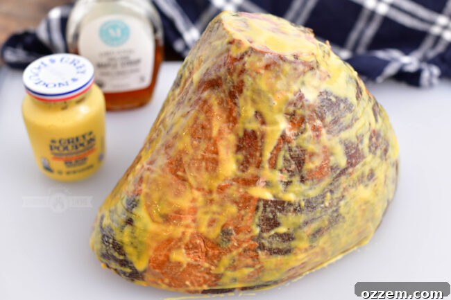 A whole smoked ham, beautifully coated in a maple Dijon mixture, rests on a cutting board, ready for the smoker, showcasing the initial prep stage.