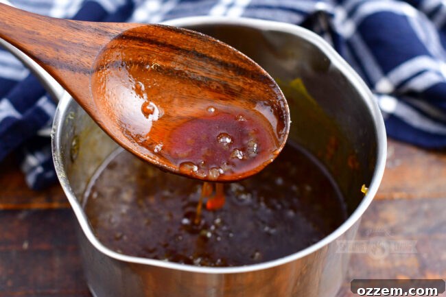 A silver sauce pot, filled with a rich, amber glaze, is shown with a spoon scooping some of the delicious mixture, ready to be applied to the smoked ham.