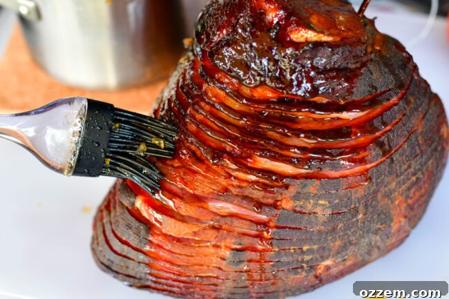 A silicone brush is generously applying a rich, golden glaze onto a smoked ham, showcasing the process of creating a caramelized, flavorful crust.