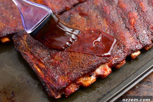 A close-up of cooked ribs being brushed with a rich BBQ sauce, creating a glossy, irresistible finish.
