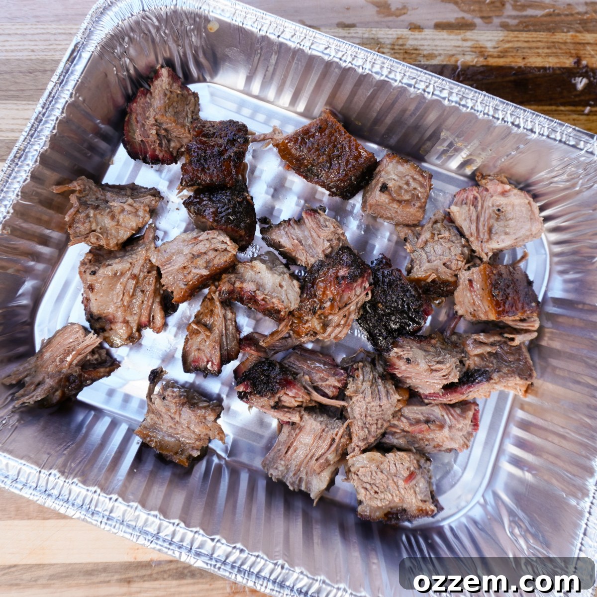 Cubed brisket neatly arranged in a foil pan, ready for seasoning and saucing