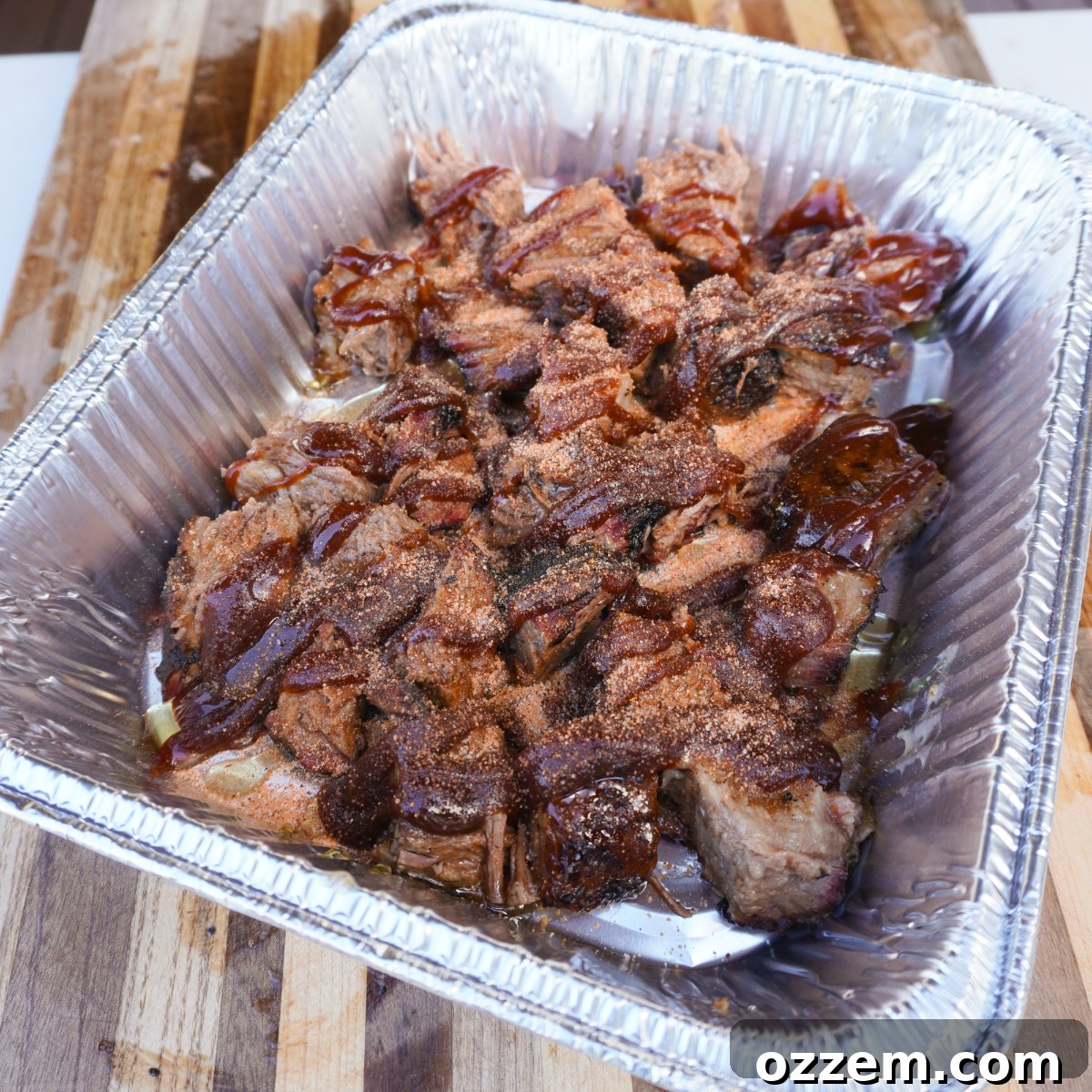 Seasoned and sauced brisket burnt ends, glistening in the pan with a rich BBQ mixture