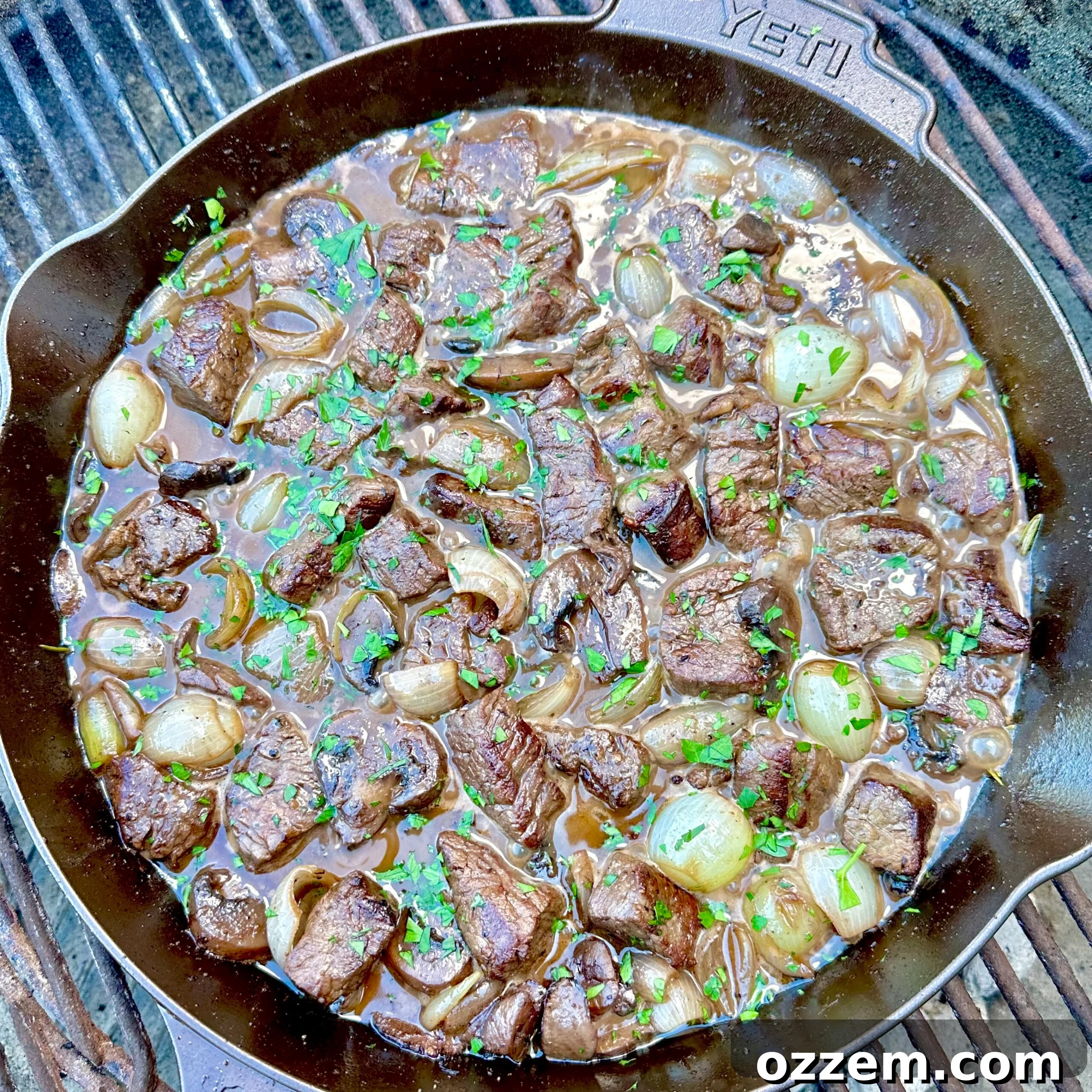 Perfectly seared beef tenderloin tips simmering in a rich red wine sauce in a cast iron skillet, garnished with fresh herbs.