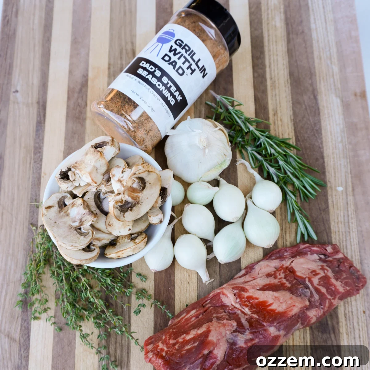 Arrangement of fresh ingredients including beef tenderloin tips, mushrooms, pearl onions, garlic, fresh rosemary and thyme.