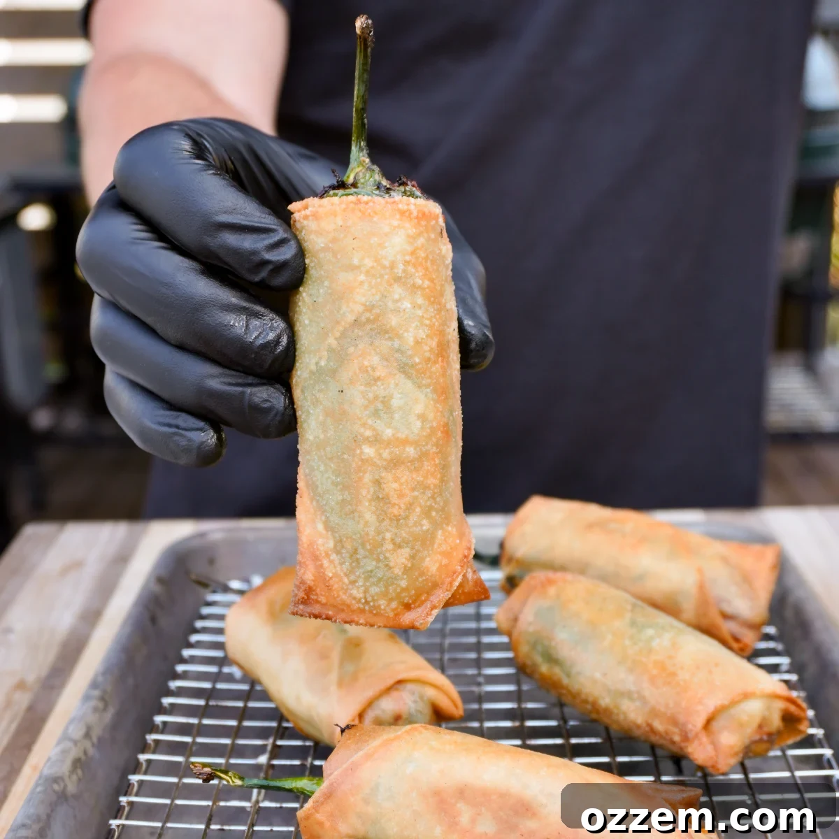 Crispy Jalapeno Popper Lumpia 2 Deep fried jalapeno popper lumpia held vertically over a tray, showcasing its crispy exterior.