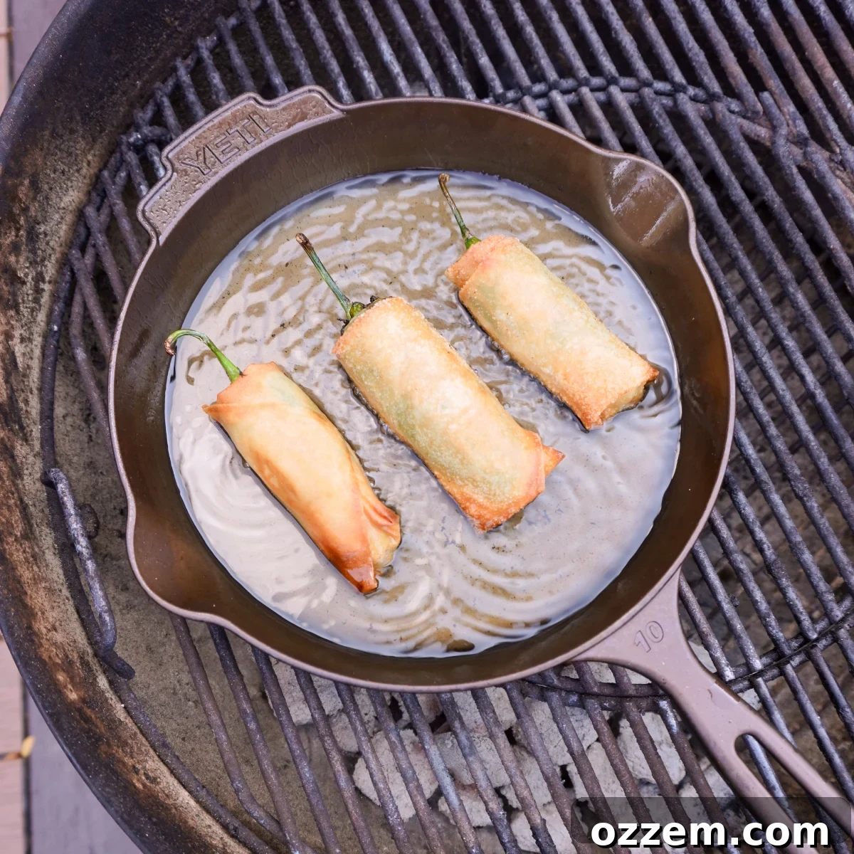 Crispy Jalapeno Popper Lumpia 13 Jalapeno popper lumpia's deep frying in a cast iron skillet on a charcoal grill.