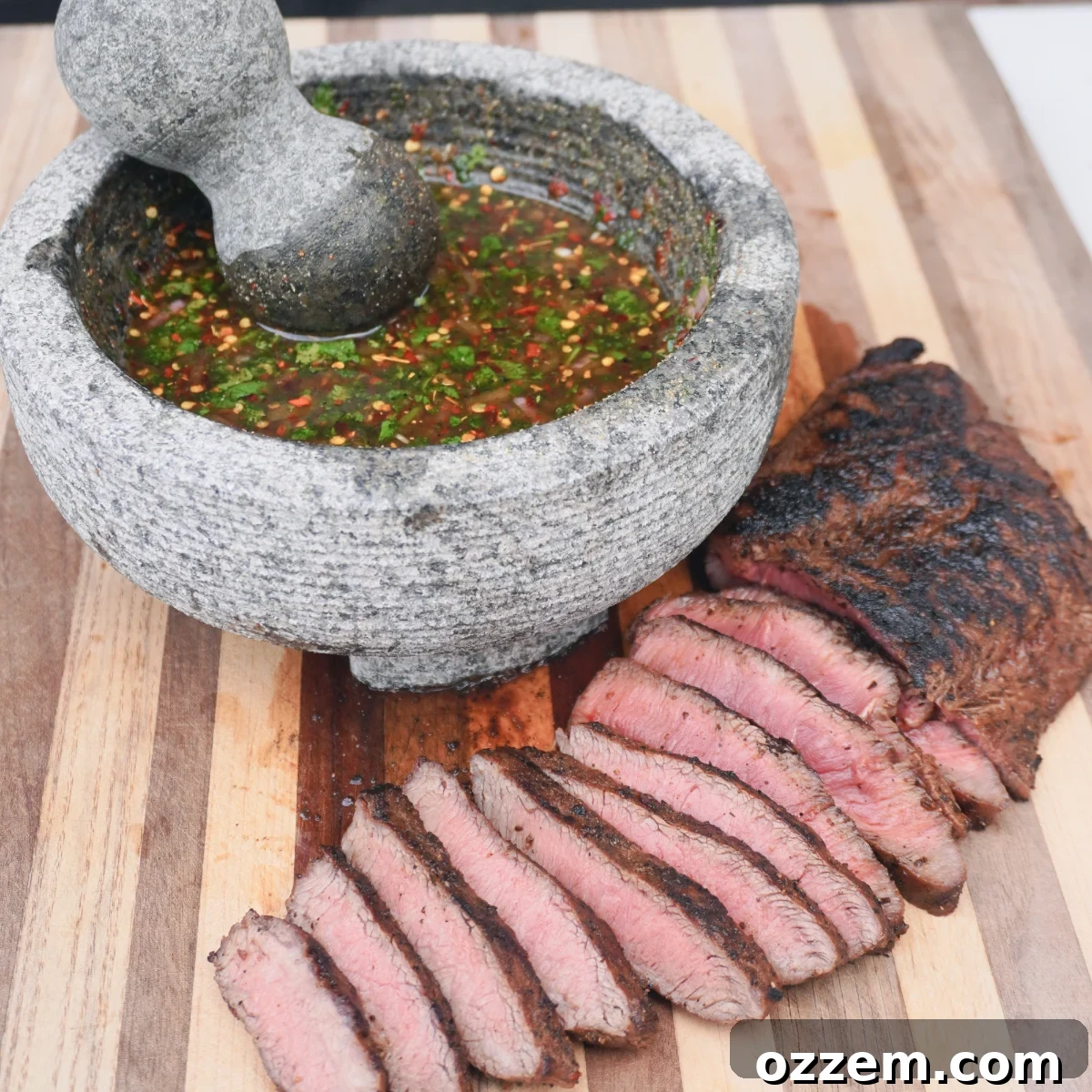 A mortar and pestle filled with crying tiger sauce, next to perfectly sliced flat iron steak.