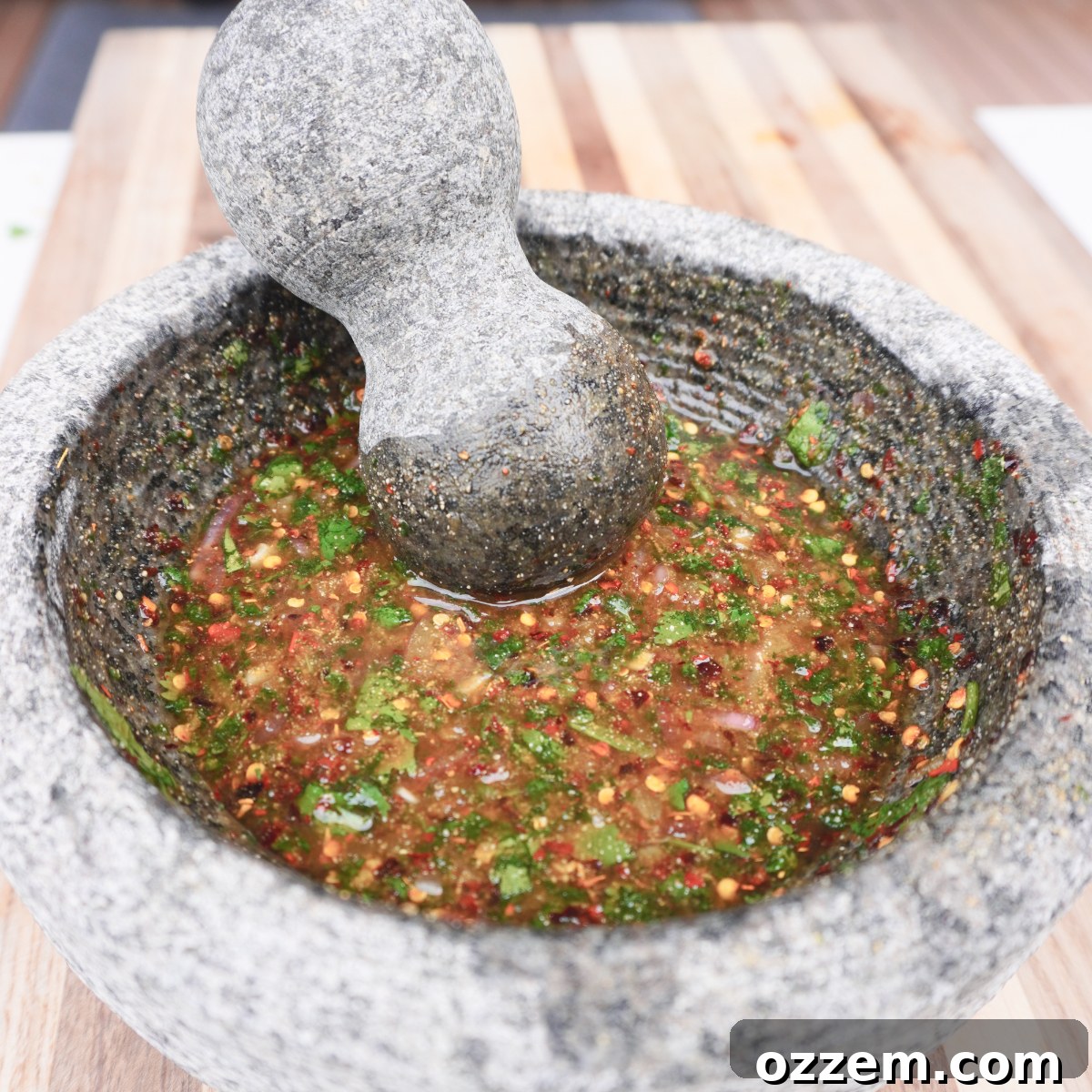 A close-up of crying tiger sauce in a mortar with a pestle, showcasing its rich texture and ingredients.