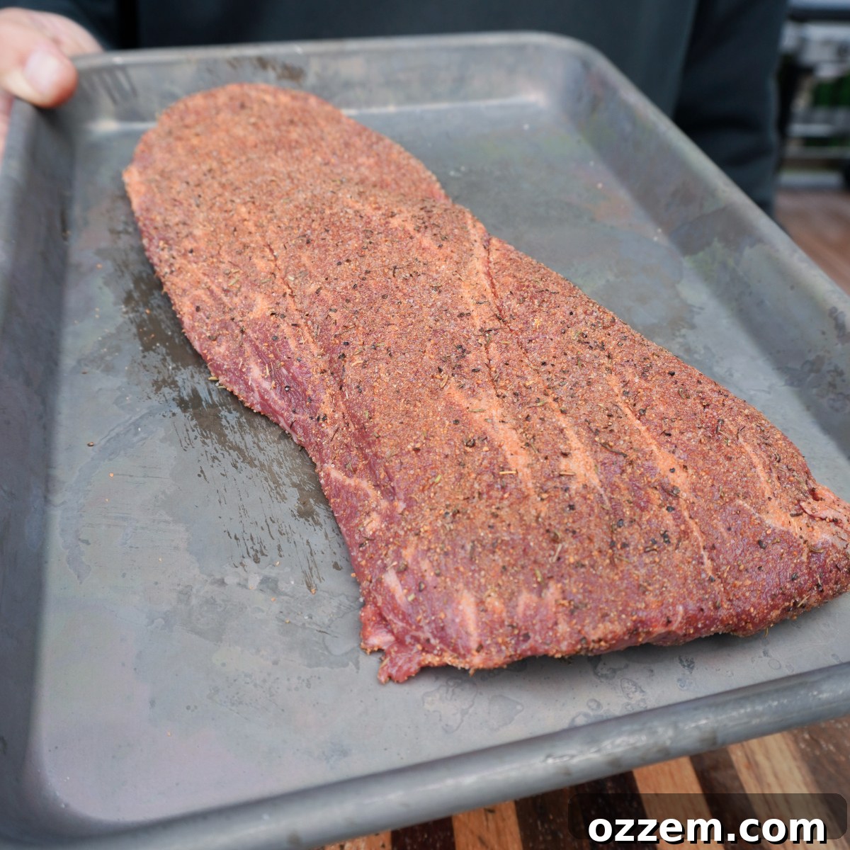 A seasoned flat iron steak resting on a sheet tray, ready for grilling.