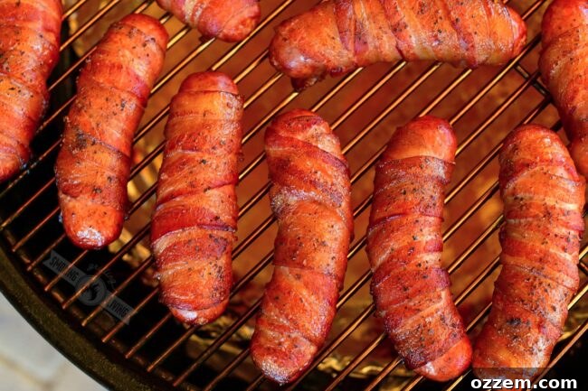 Close-up of bacon-wrapped sausages smoking on a grate inside a smoker, looking perfectly golden