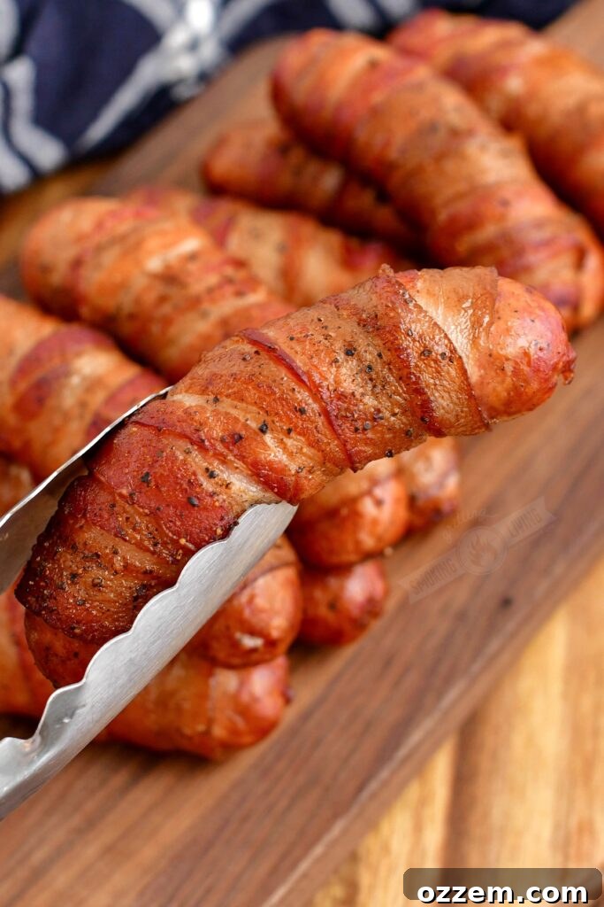 A perfectly smoked, bacon-wrapped sausage being held with metal tongs, glistening with flavor