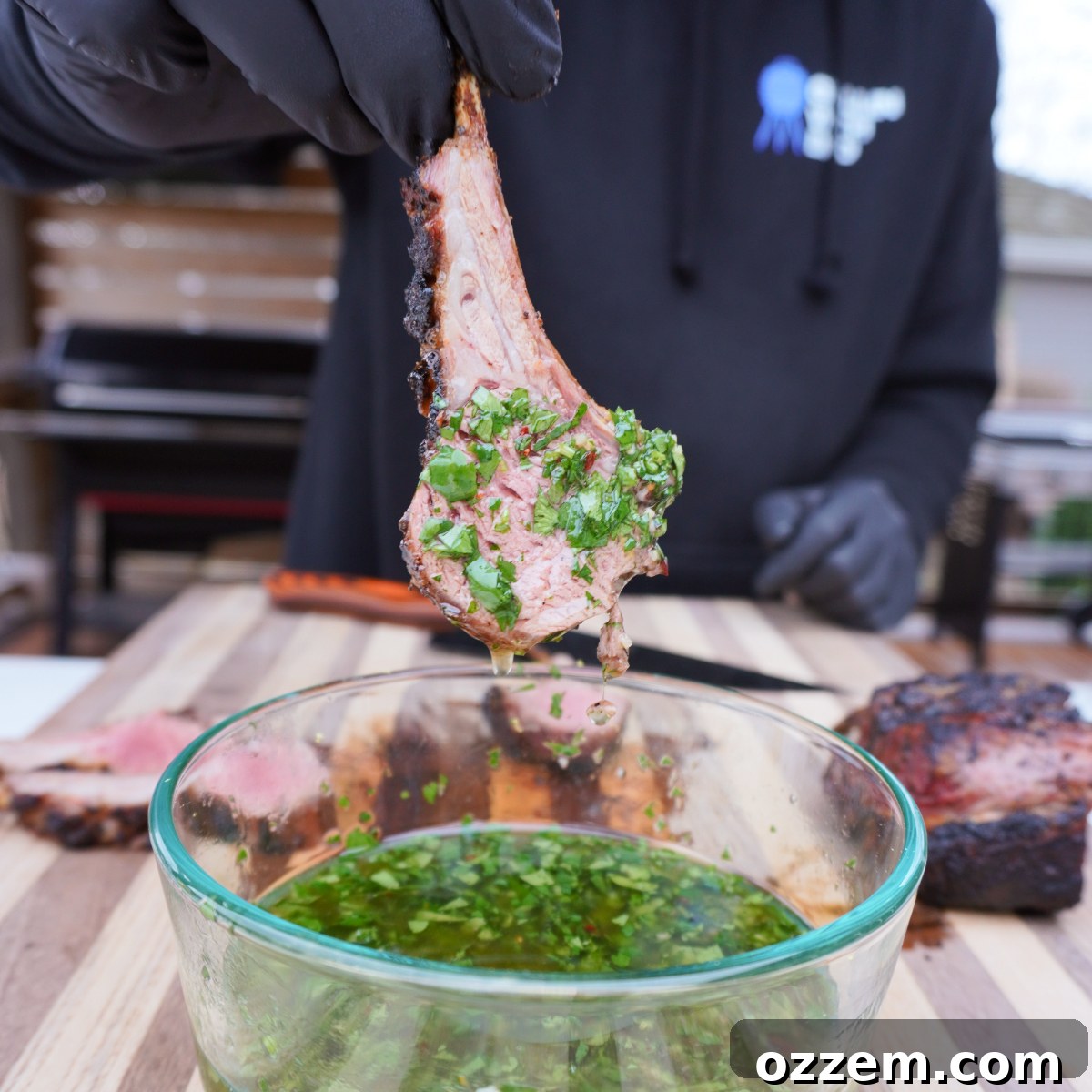 smoked and sliced rack of lamb dipped in a mint chimichuri sauce from a clear bowl, ready to be enjoyed.