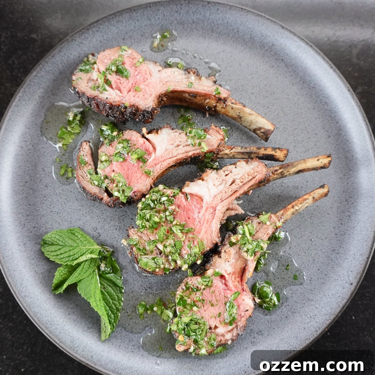 smoked lamb chops with mint chimichurri sauce on a grey serving plate with a side of fresh mint leaves, showcasing perfect doneness.