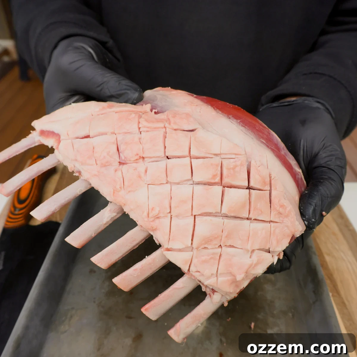 scored trimmed raw rack of lamb showed off by hands, highlighting the diamond pattern.