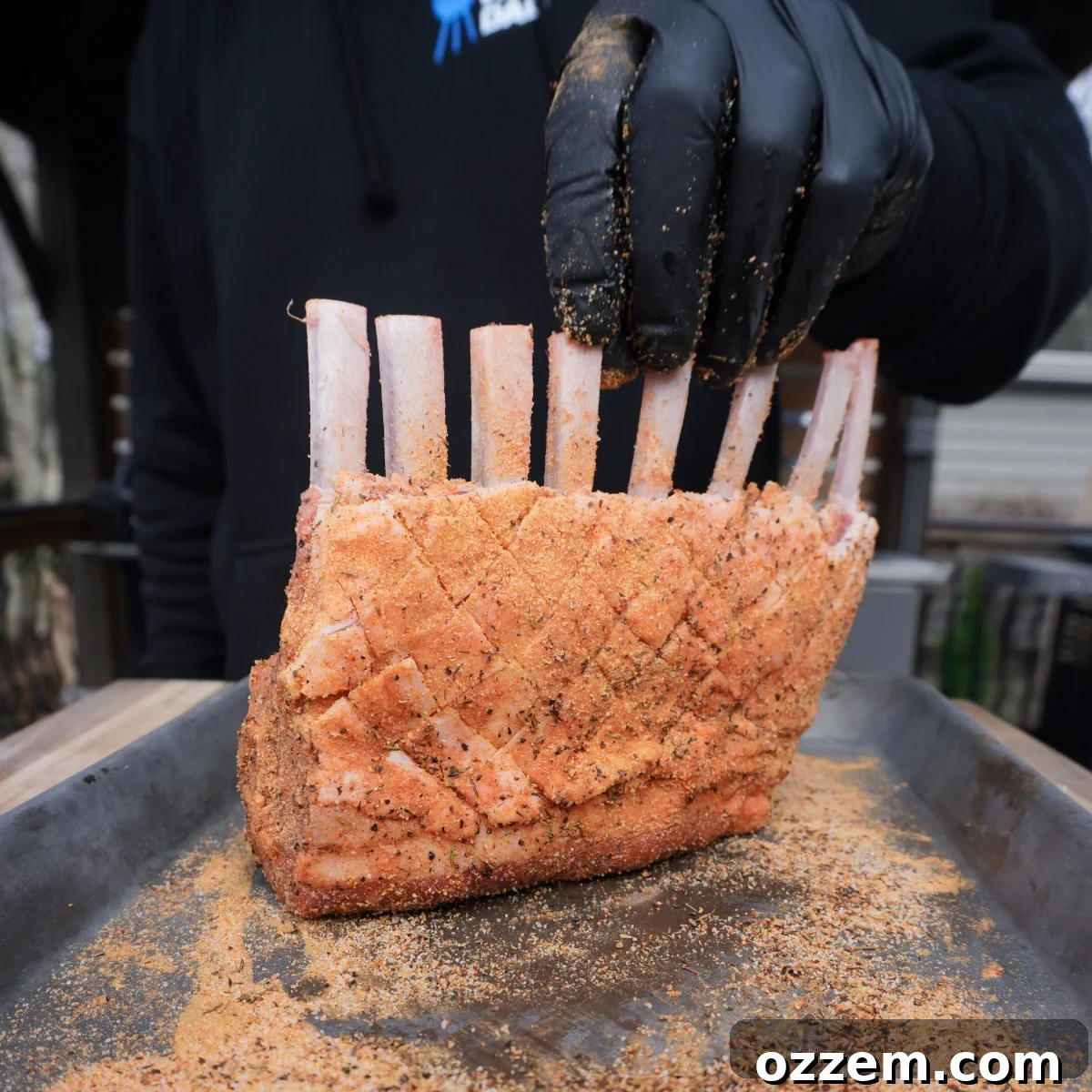 seasoned raw rack of lamb upright on a metal tray, ready for the grill.