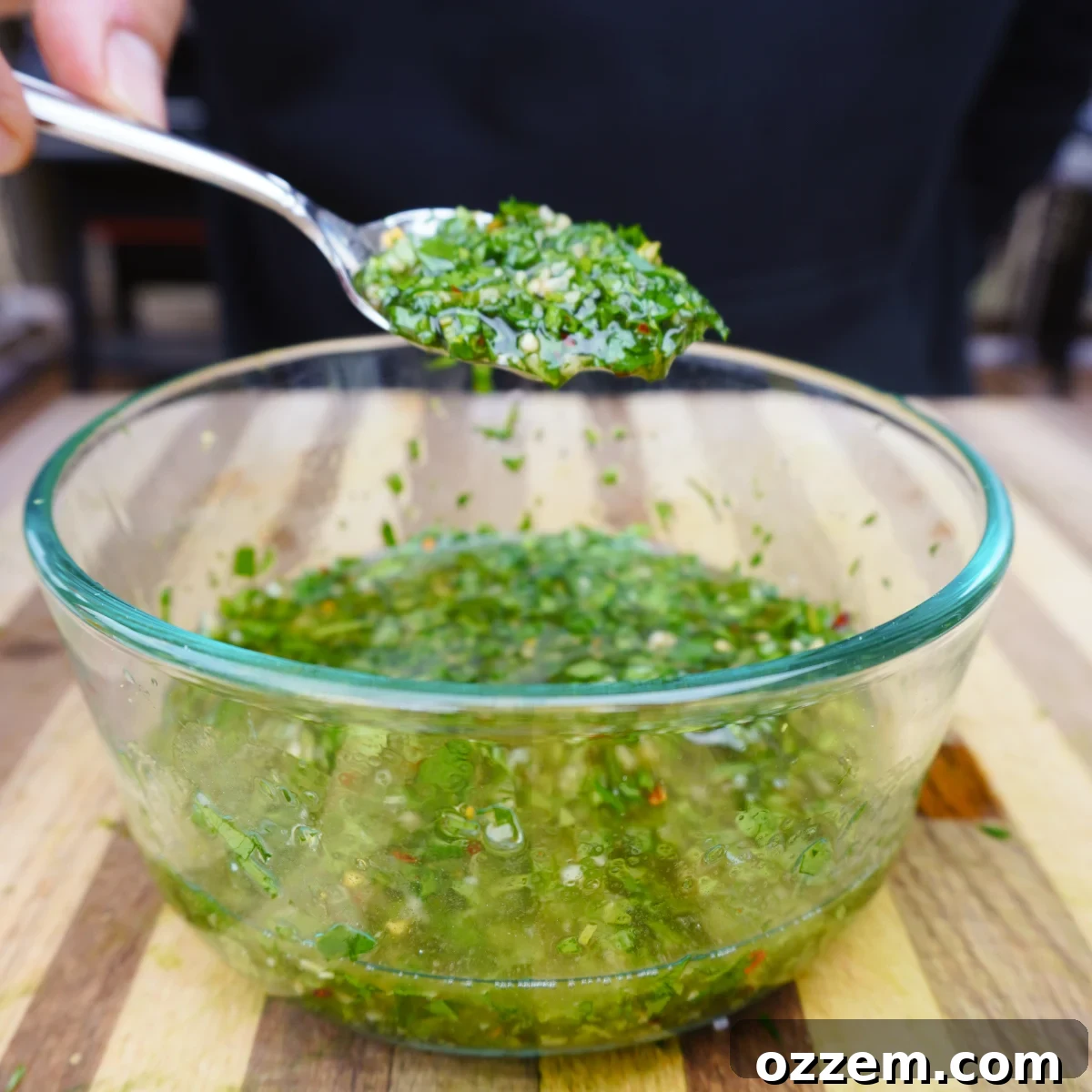 mint chimichurri sauce in a glass bowl scooped up with a small spoon, showcasing its chunky texture.