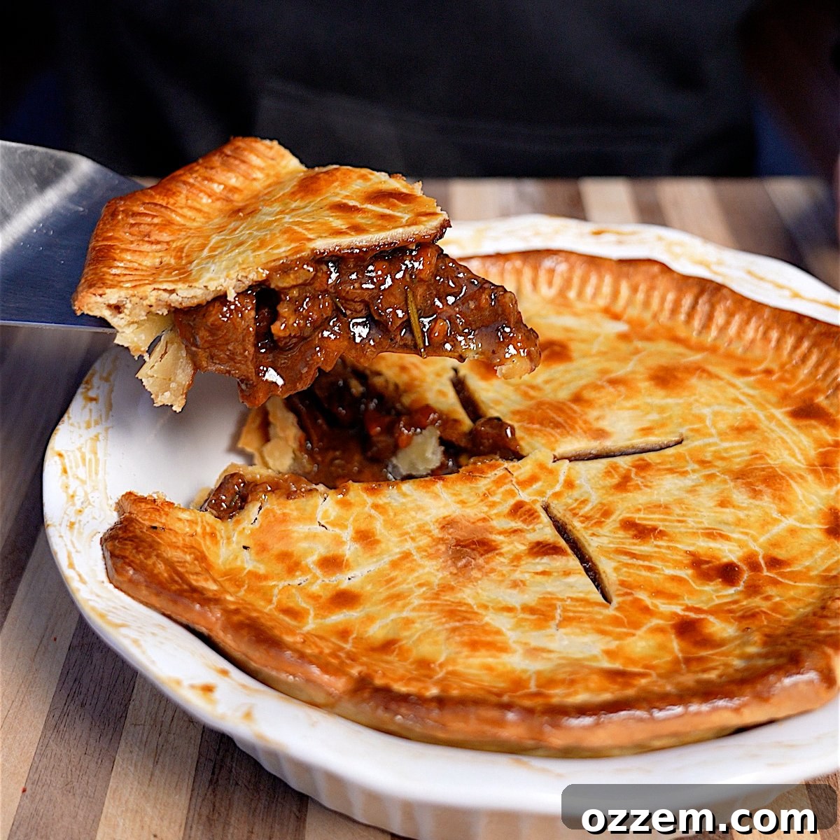 A perfectly baked smoked meat pie with a slice cut out, revealing the rich, meaty gravy filling and tender chunks of steak within a golden-brown crust.