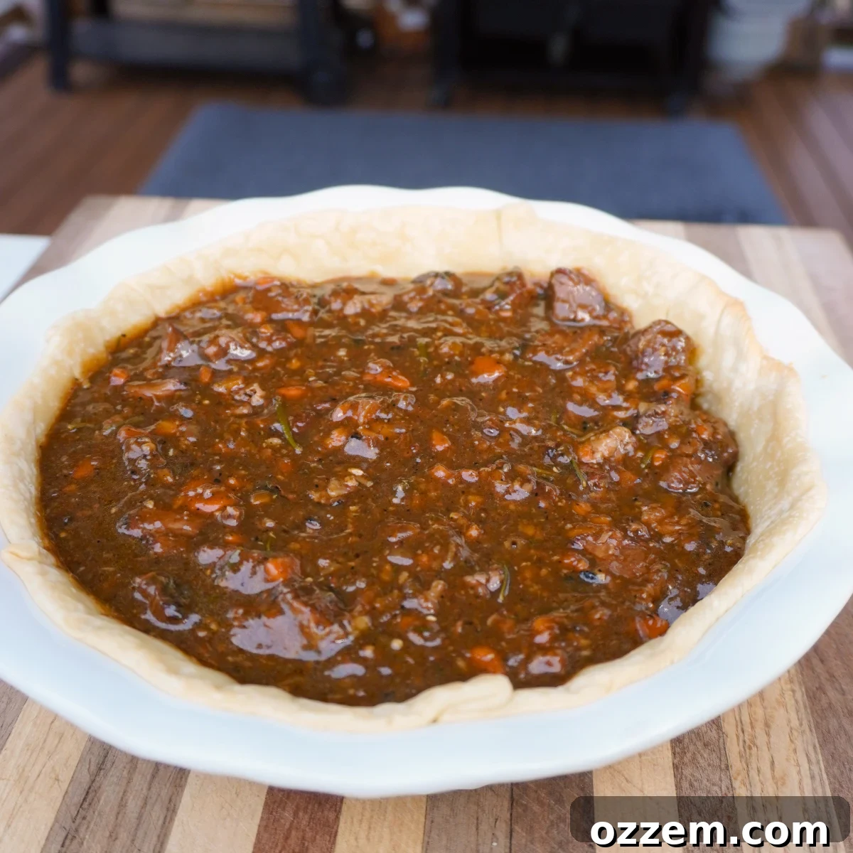 A blind-baked bottom pie crust in a white ceramic pie dish, filled with the rich, meaty gravy, ready for the top crust.