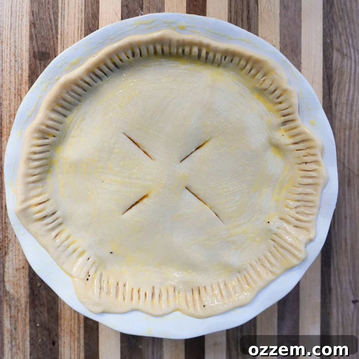A top pie crust with decorative slits, brushed with egg wash, covering the filling in a pie dish and ready for grilling or baking.