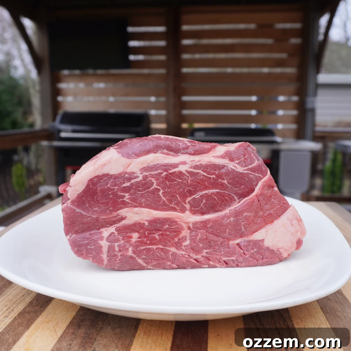 Raw chuck roast liberally seasoned with spices, resting on a white plate atop a rustic wooden cutting board, ready for the smoker.