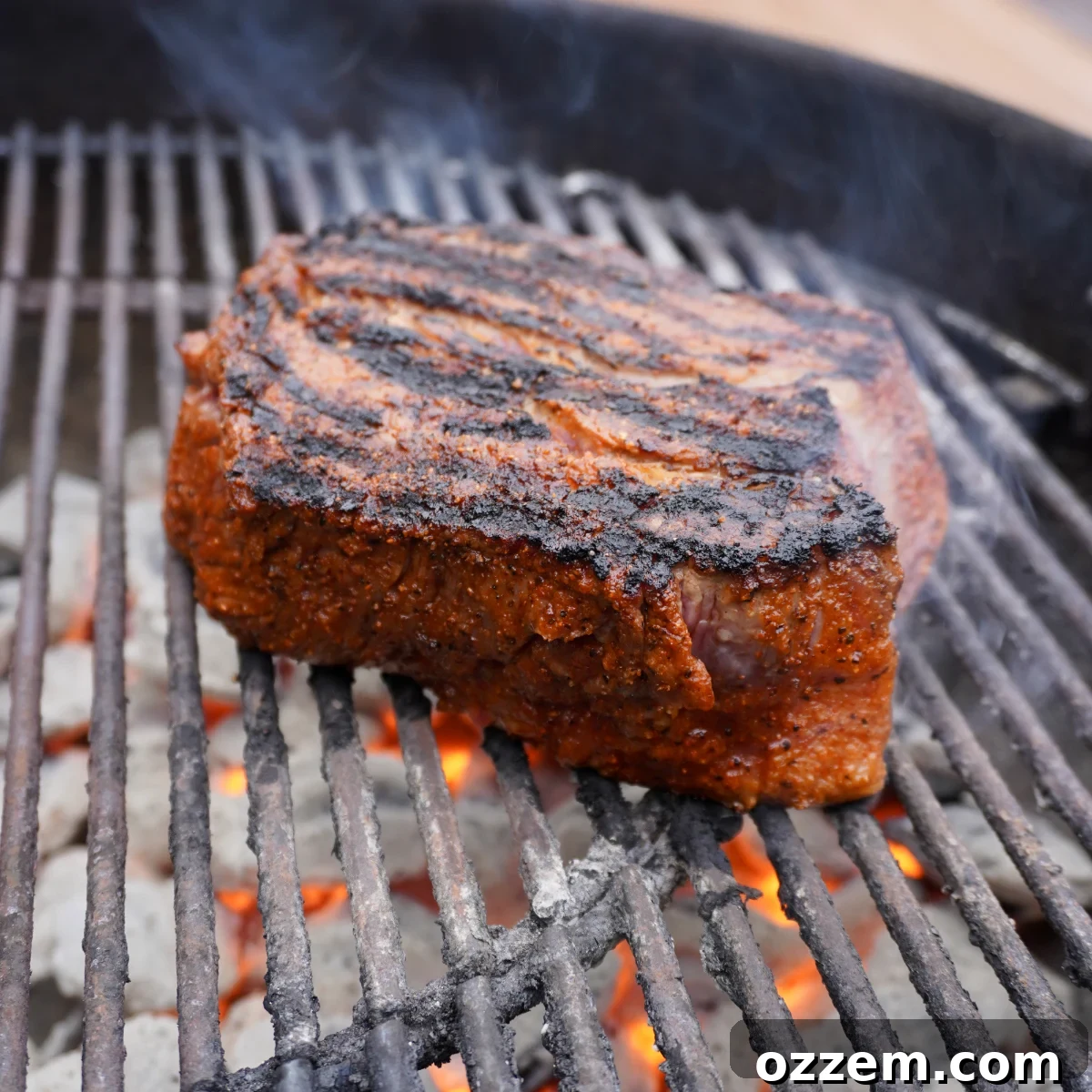 A perfectly seared chuck roast placed on clean grill grates, positioned over hot charcoal for smoking.