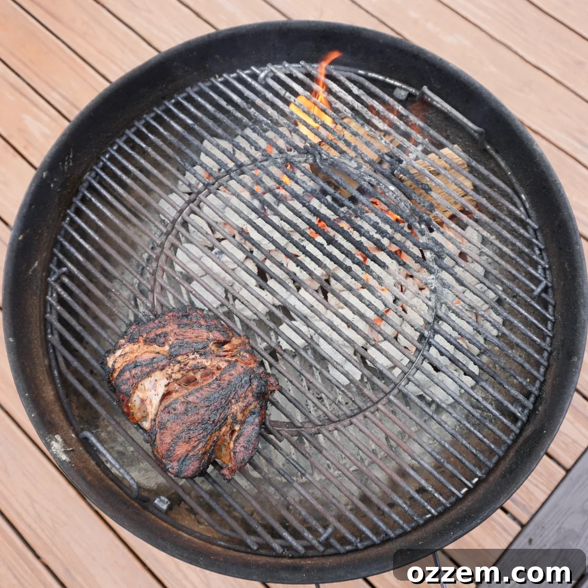 A charcoal grill set up for dual zone cooking, with hot charcoal and wood chunks on the right side generating smoke, and a chuck roast gently smoking on the left.